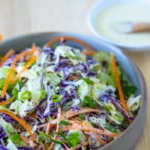 coleslaw in bowl with extra dressing on the side
