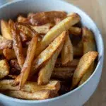 Side view of golden, crispy air fryer chips in a white bowl, showing crunchy texture