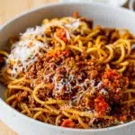 Side view of Bolognese sauce with pasta with grated cheese and red chilli served on a small saucer on the side.