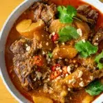 Top view of a big bowl of Massaman beef curry with potatoes in a rich, creamy sauce.
