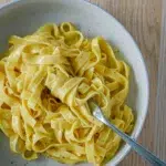 A plate of authentic fettuccine Alfredo with a twisted forkful, topped with freshly cracked black pepper.