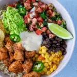 Close-up of Colorful chicken burrito bowl filled with seasoned chicken, rice, black beans, corn, diced tomatoes, and avocado, garnished with cilantro