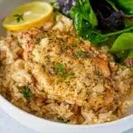 Bowl of lemon herb chicken and rice, showcasing tender chicken thighs garnished with fresh herbs and lemon slices, served over fluffy rice.
