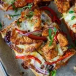 Close-up of a cheesy chicken flatbreads topped with grilled chicken pieces, red bell peppers, red onions, and fresh parsley on a baking tray