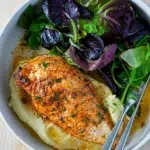 A bowl of Baked garlic chicken breast cooked at high heat for tenderness and juiciness, served with mashed potato and fresh herbs