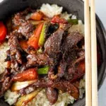 A bowl of black pepper beef stir-fry featuring tender beef slices, colorful bell peppers, and green onions, served in a rich black pepper sauce and chopsticks on side