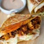 Close-up of folded nacho wraps filled with seasoned meat and cheese, grilled to a crispy golden brown, served on a wooden board