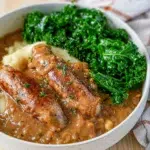 A bowl of Sausages served with homemade onion gravy, garnished with fresh herbs, and accompanied by mashed potatoes