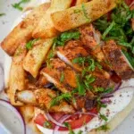 A close-up of Chicken Shawarma served with garlic yogurt sauce, garnished with fresh parsley and onions