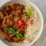 Coconut Beef Curry served in a bowl with fresh herbs and a side of rice