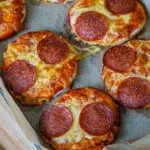 Freshly baked mini pizzas on a tray, topped with shredded mozzarella cheese, and pepperoni.