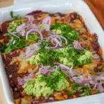 Delicious cheesy chicken enchiladas topped with creamy avocado, onion, and fresh herbs.