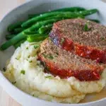 Tangy tomato-glazed meatloaf served with creamy mashed potatoes and green beans.