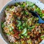 Overhead view of a bowl of rice with a spoon, topped with tuna and avocado.