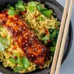 Overhead shot of a bowl of glazed miso salmon with ramen noodles, served with chopsticks.
