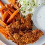 Close-up of Southern 'Fried' Baked Chicken Strips, golden-brown and crispy, served with sweet potato wedges and a side of sour cream for dipping.