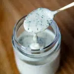 Spoon dripping homemade ranch dipping sauce into a glass jar.