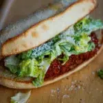 Close-up of a Crispy Chicken Caesar Sandwich with golden fried chicken, lettuce, and Caesar dressing in a toasted bun.