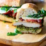 Side view of crispy chicken pesto sandwich cut in half, showing layers of chicken, pesto, and melted cheese