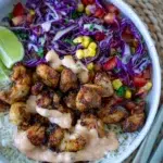 Overhead view of Peri Peri chicken and rice on a plate, set on a mat with chopsticks.