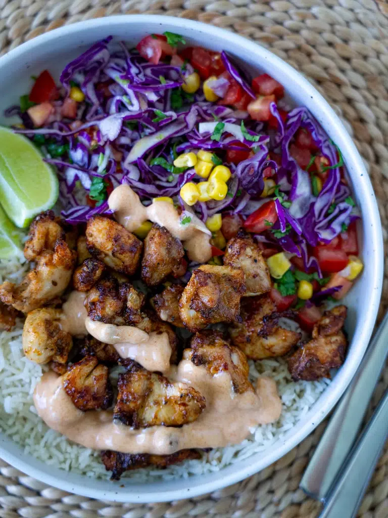 Overhead view of Peri Peri chicken and rice on a plate, set on a mat with chopsticks.