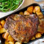 Top view of Rosemary Garlic Lamb shoulder served on a tray with gravy and leafy green salad.