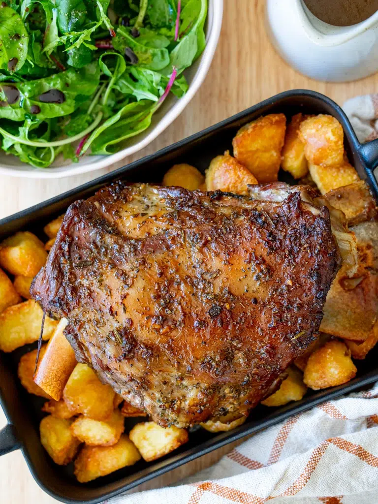 Top view of Rosemary Garlic Lamb shoulder served on a tray with gravy and leafy green salad.