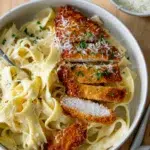 Top view of sliced crispy chicken on fettuccine Alfredo with a fork resting beside the plate