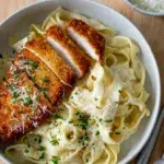 Top view of crispy chicken fettuccine Alfredo plated with a creamy sauce and garnish.