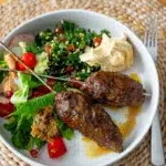 Plated lamb kofta alongside vibrant fattoush salad and creamy hummus.