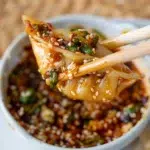 dumpling just dunked in sauce being held by chopsticks