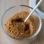 Glass jar filled with homemade chicken salt seasoning and a spoon scooping the blend, placed on a wooden surface