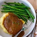 Overhead shot of pork chop with homemade gravy, mashed potatoes, and green beans – comforting final plated dish