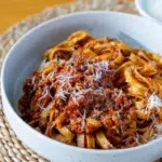 Bowl of fettuccine pasta topped with hidden vegetable Bolognese sauce and freshly grated Parmesan cheese, served on a woven placemat.