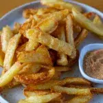 Crispy oven fries served with a side of chicken salt on a white plate