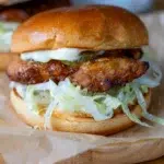Close-up of a hot honey crunch chicken burger with crispy fried chicken, shredded lettuce, pickles, and mayonnaise in a soft brioche bun.