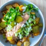 Top view of a Loaded Potato Big Mac Bowl with crispy potatoes, seasoned beef, shredded lettuce, pickles, diced onions, and special sauce, served in a speckled ceramic bowl.