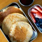 Bird’s eye view pancakes in stainless steel lunchbox with fruit and maple syrup on side