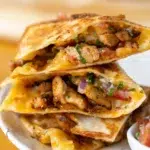 Close-up of cheesy chicken quesadillas stacked on a plate, filled with seasoned chicken, pico de gallo, and melted cheese