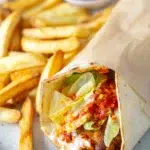 Close-up of Portuguese-style chili chicken wrap with lettuce, sauce, and fries on a plate