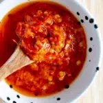 Close-up of Portuguese-style chili sauce in a small bowl with a wooden spoon dipped in