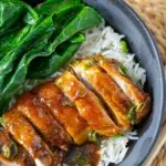Bowl of honey garlic chicken and rice with fresh greens, paired with chopsticks for serving.