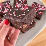 Finished Valentines Day brownie being held in hand above the platter of brownies