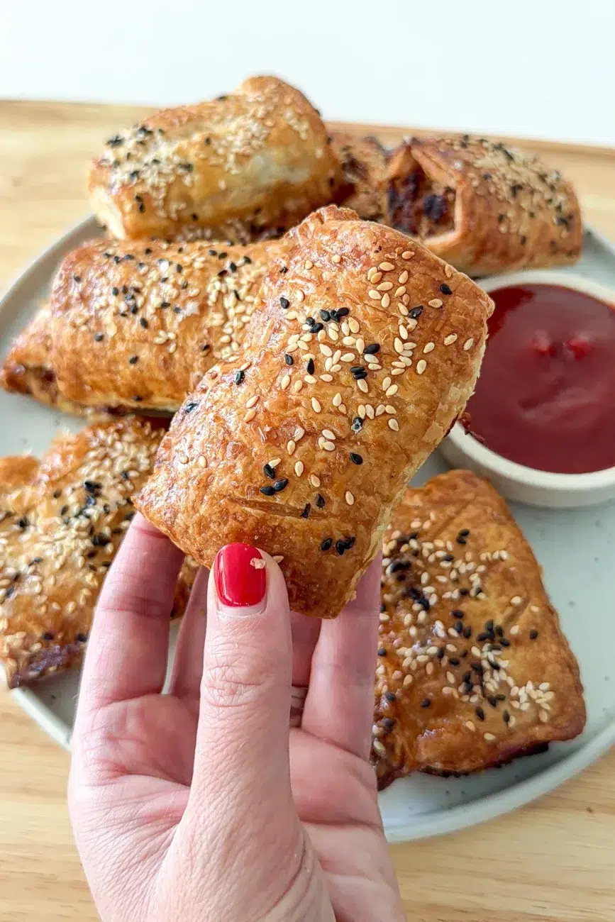 sausage roll being held in hand in front of platter