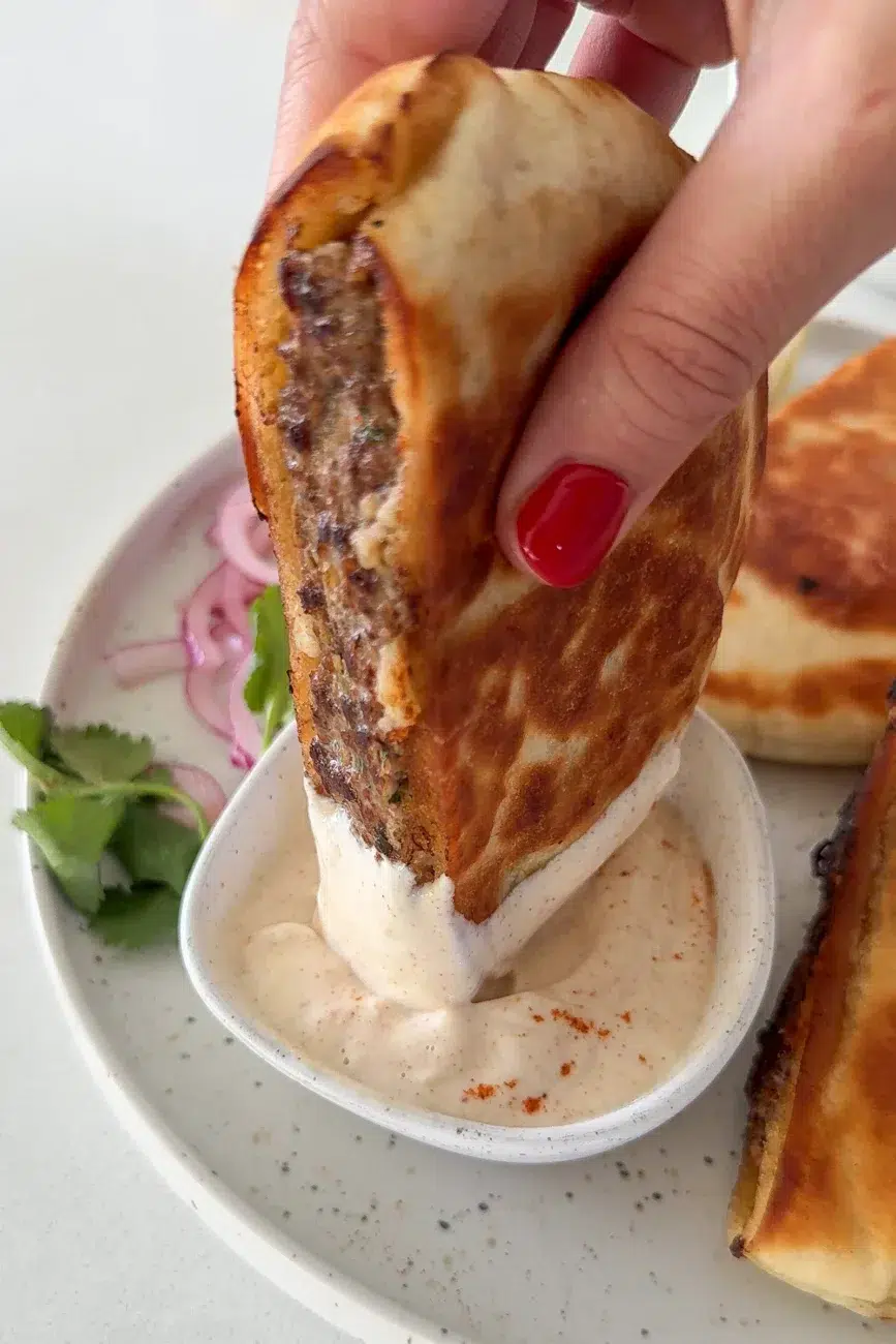 stuffed pita being dipped into creamy garlic–tahini dip