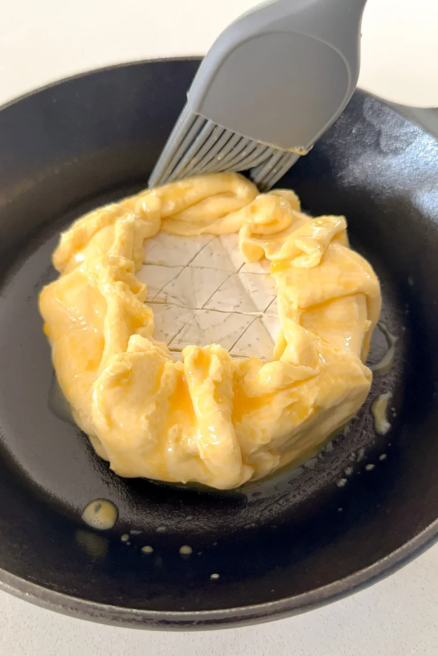 Brie encased in pastry being brushed with egg wash