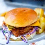 Crispy fried chicken burger with ranch slaw, cheese and pickles on a toasted brioche bun, served with crispy potato wedges