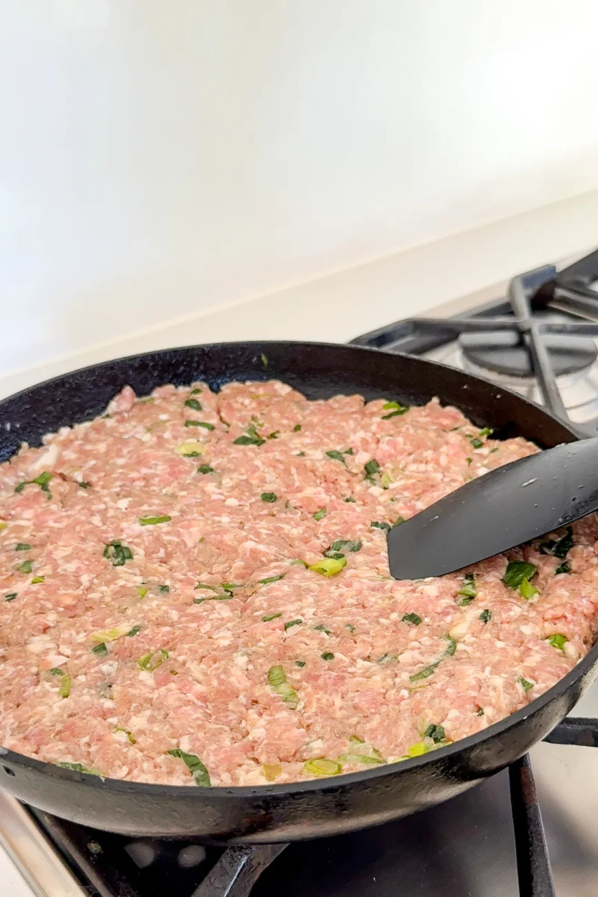 Pork mixture spread in pan ready to be topped with dumpling wrappers