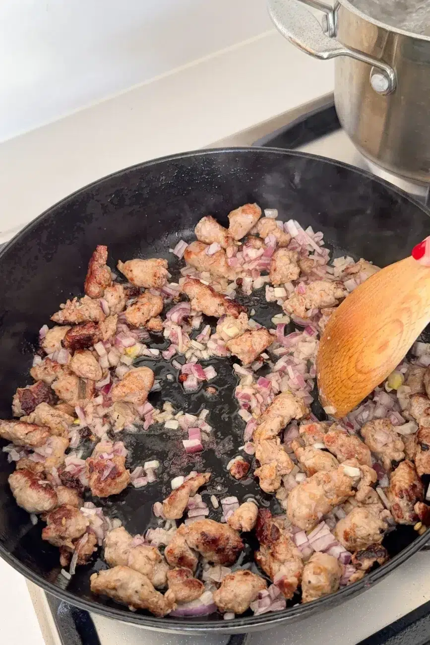 Sausages and onions being fried in pan