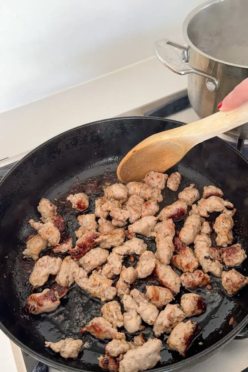 Sausages in pan being cooked until golden and crispy